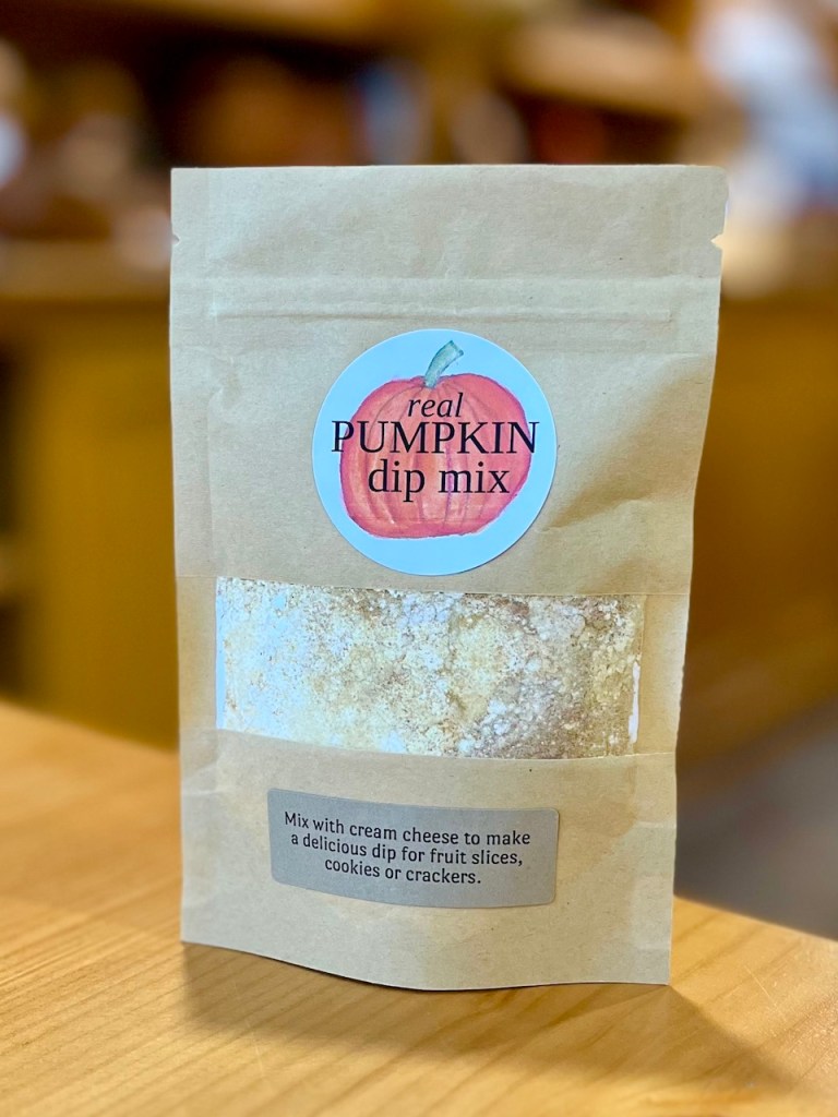 A packet of real pumpkin dip mix on a wooden surface, featuring a colorful label with a pumpkin illustration and instructions for mixing with cream cheese.