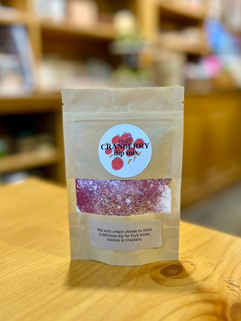 A package of real cranberry dip mix displayed on a wooden table, featuring instructions to mix with cream cheese for a delicious dip suitable for fruit slices, cookies, or crackers.