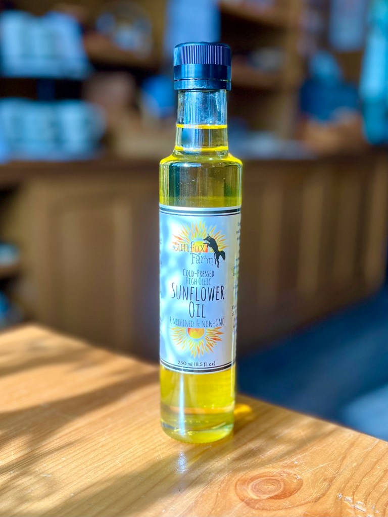 A bottle of cold-pressed high oleic sunflower oil, labeled as unrefined and non-GMO, placed on a wooden surface.
