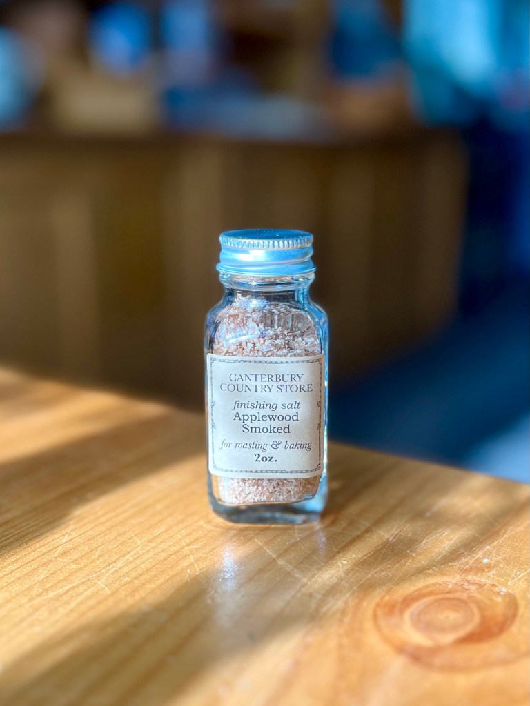 Glass jar of Applewood smoked finishing salt labeled 'Canterbury Country Store', placed on a wooden surface with soft lighting.