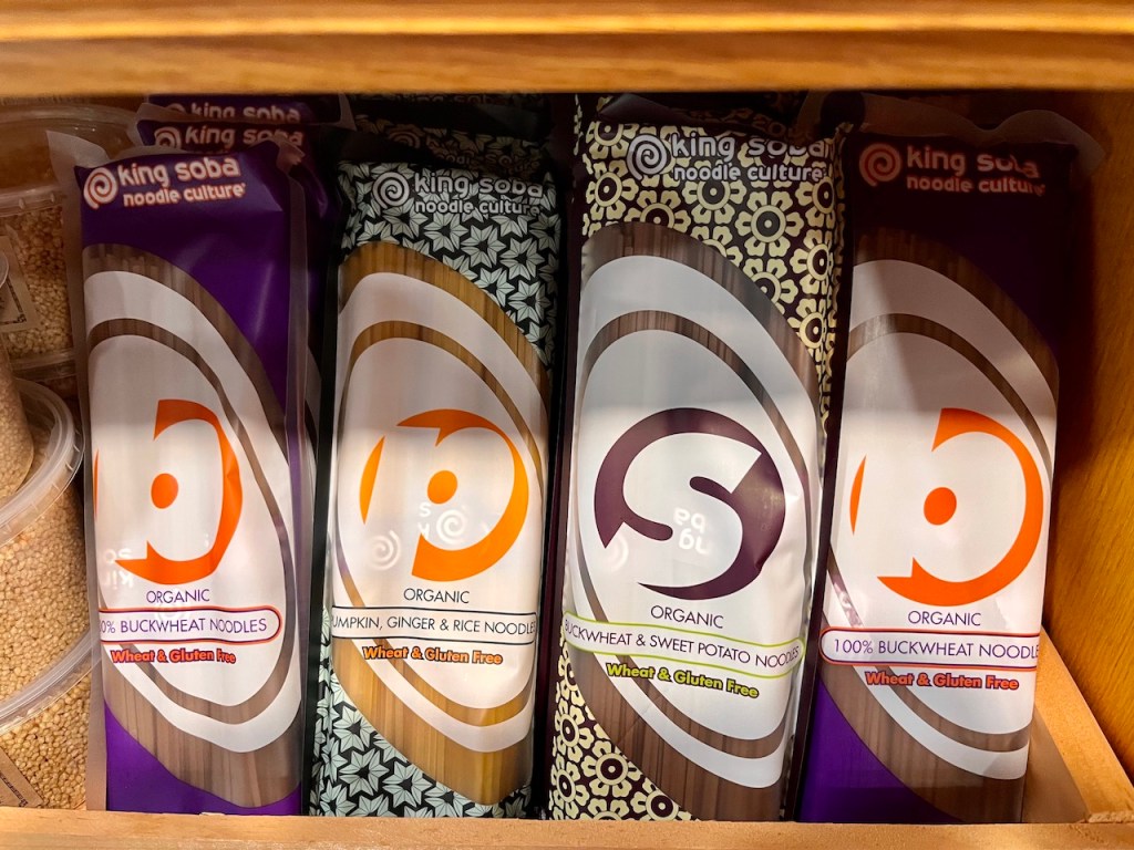 Shelf displaying various types of organic buckwheat noodles in colorful packaging.