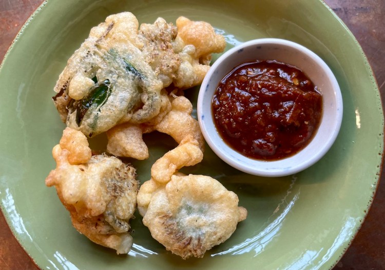 A plate of crispy herb fritters served with a small bowl of dipping sauce.