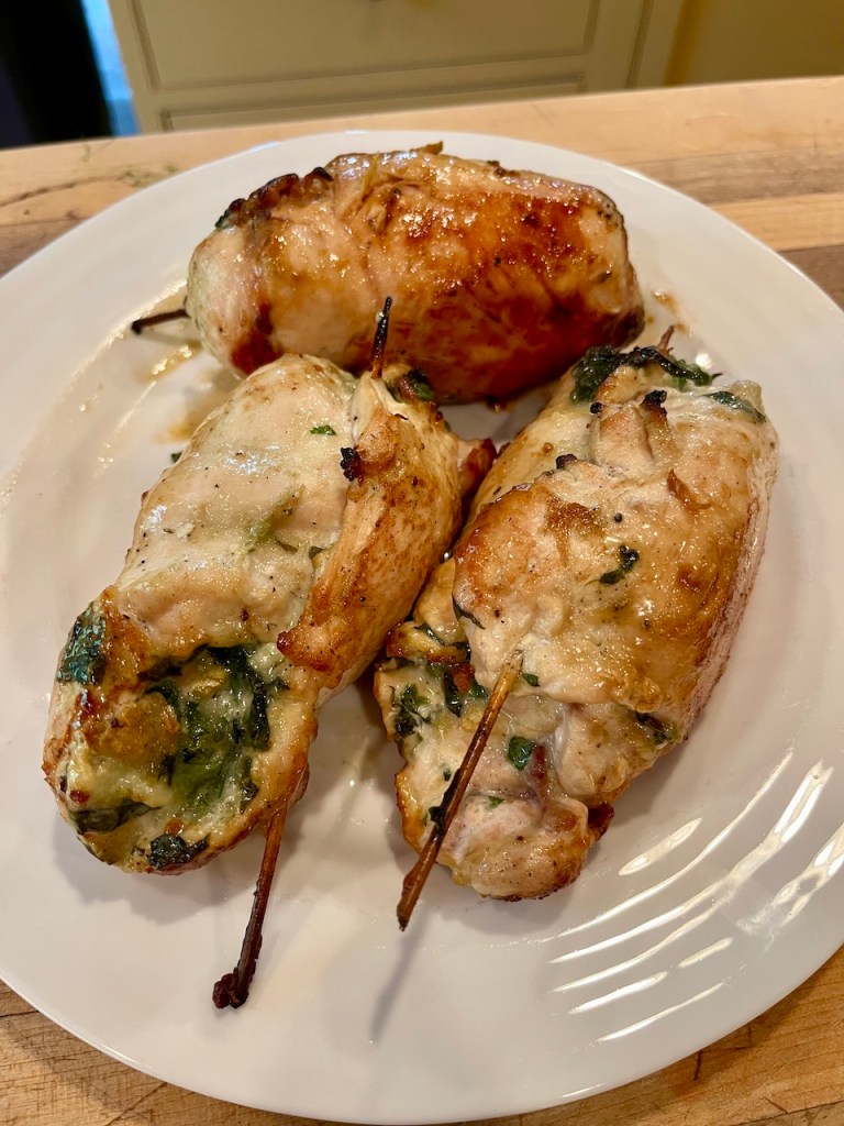 Three rolled and stuffed chicken breasts on a white plate, garnished with herbs.