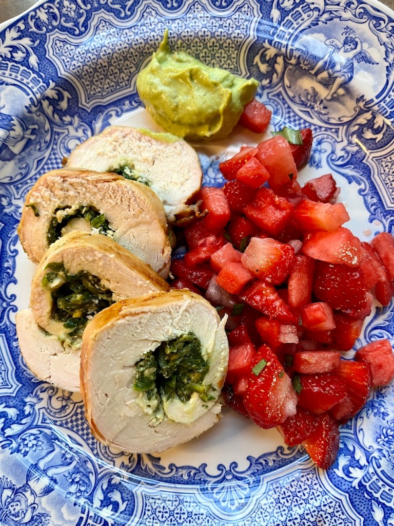 Plate featuring rolled and sliced chicken breast stuffed with spinach and cheese, accompanied by a fresh strawberry-watermelon salsa and a serving of guacamole.