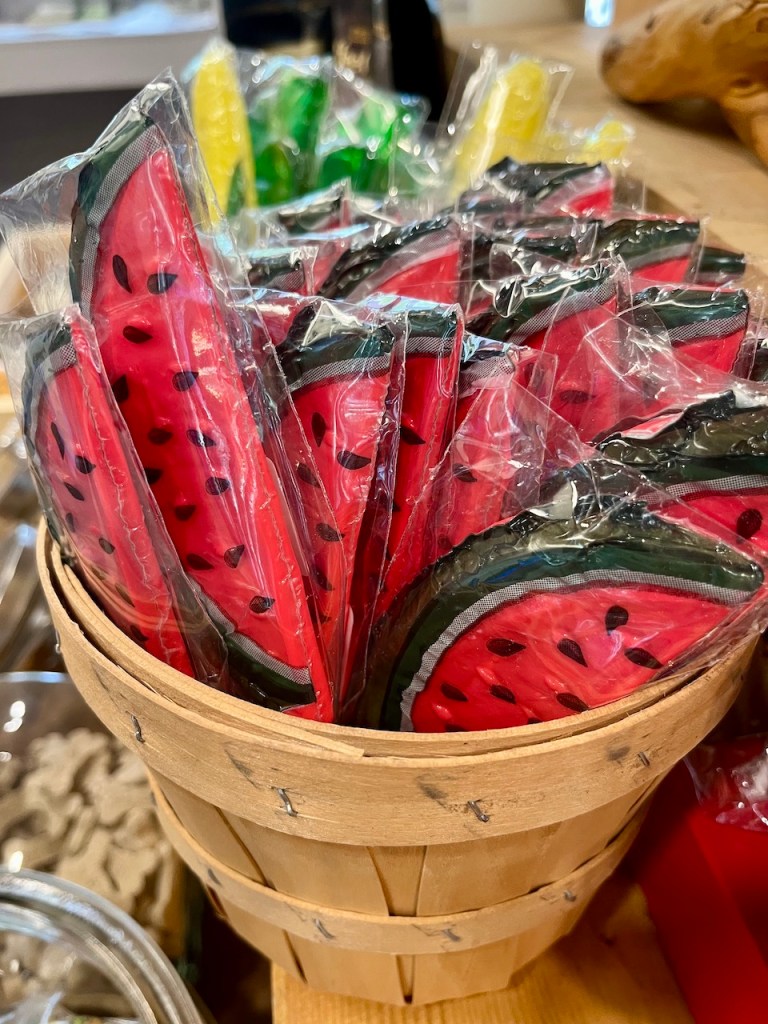 A wooden basket filled with individually wrapped watermelon-shaped candy, showcasing vibrant red and green colors.