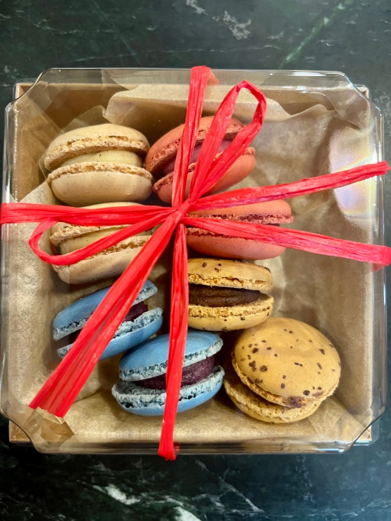 A box of colorful macarons in various flavors, neatly arranged and tied with a red ribbon.