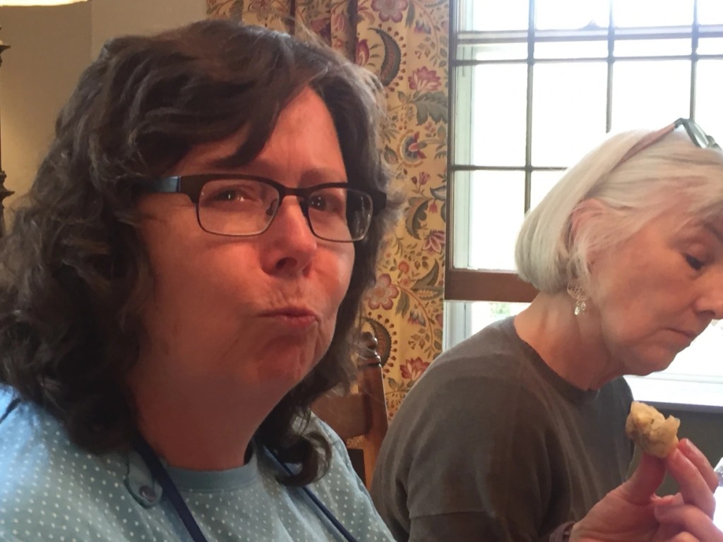 Two women enjoying food at a table, with one woman making a playful expression while the other focuses on her meal.