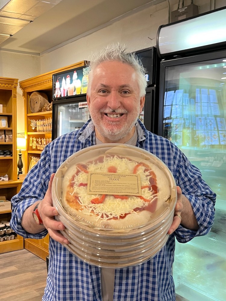 Man smiling while holding a stack of pizza boxes in a food store.