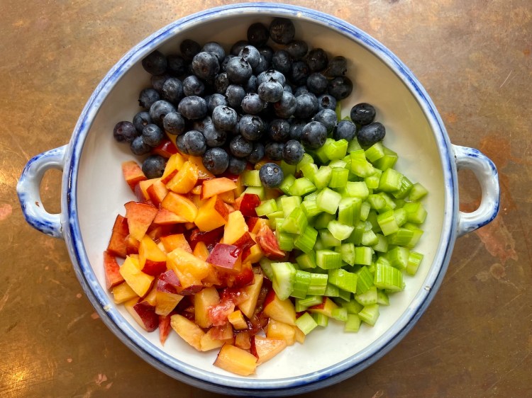 Bowl filled with cubed yellow nectarines, chopped celery, and blueberries, arranged for a fruit salad.