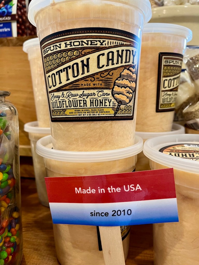 A jar of spun honey cotton candy with a label stating 'Made in the USA since 2010' placed among other jars on a wooden display.