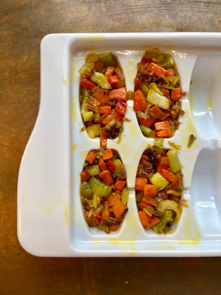 A tray filled with diced cooked mirepoix, consisting of carrots, celery, and onions, displayed in separate compartments.