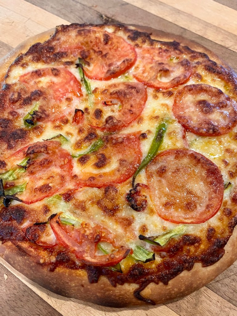A freshly baked pizza topped with sliced tomatoes and green peppers, presented on a wooden surface.