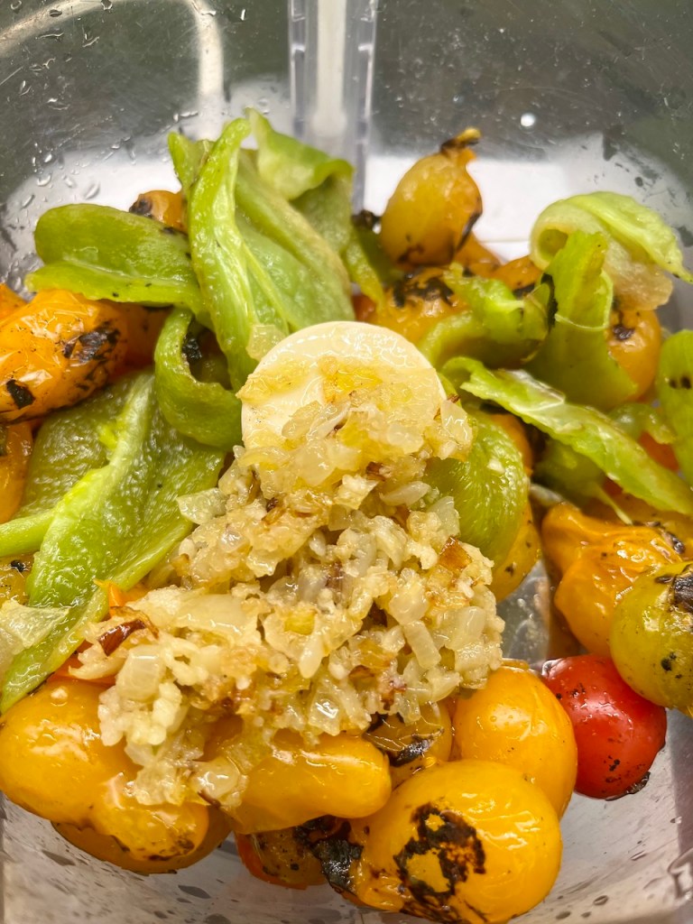 A close-up of blended fire-roasted vegetables, including yellow and red cherry tomatoes, green peppers, and chopped onions in a mixing container.