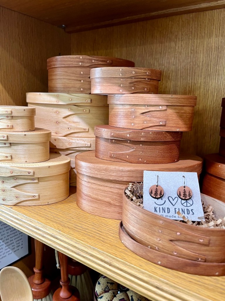 A collection of beautifully crafted wooden Shaker boxes in various sizes and finishes, displayed on a wooden shelf, with a tag stating 'Kind Finds'.