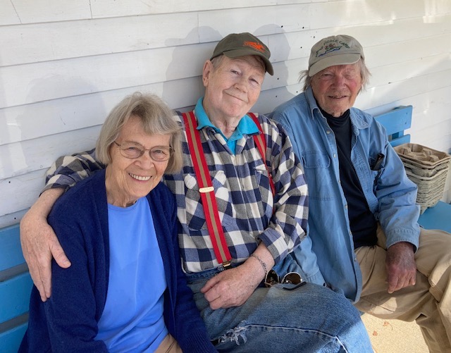 Three older adults sitting together on a bench, smiling and enjoying each other's company.
