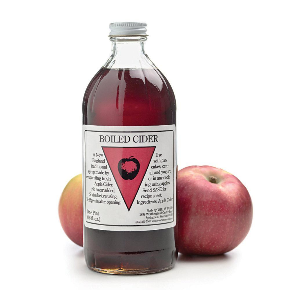 A bottle of boiled cider with a red label, featuring a drawing of an apple, alongside two fresh apples.