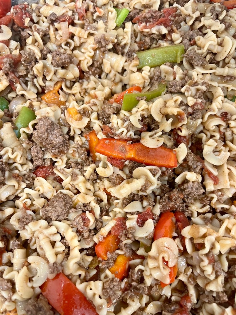 A close-up view of a mixed pasta dish featuring spiral pasta, ground beef, diced bell peppers, and chopped tomatoes, all intertwined in a savory sauce.