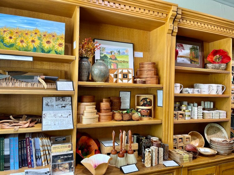 A display of handcrafted artisan products, including pottery, woodwork, and paintings on shelves, highlighting local craftsmanship and artistry.