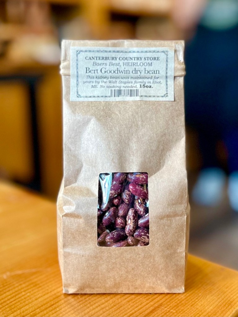 A package of Bert Goodwin heirloom dry beans from Canterbury Country Store, featuring a transparent window showcasing the beans inside. The label describes the beans as locally sourced, with no soaking required.