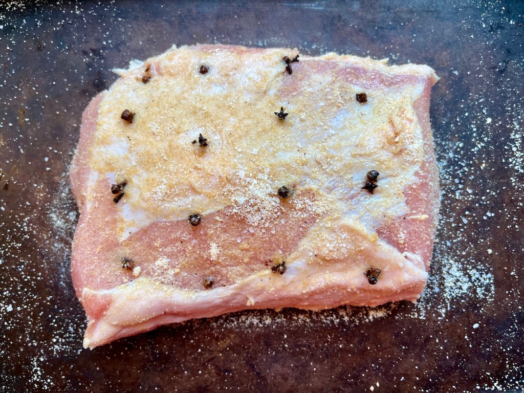 A seasoned pork loin roast with cloves and spices on a baking tray, ready for cooking.