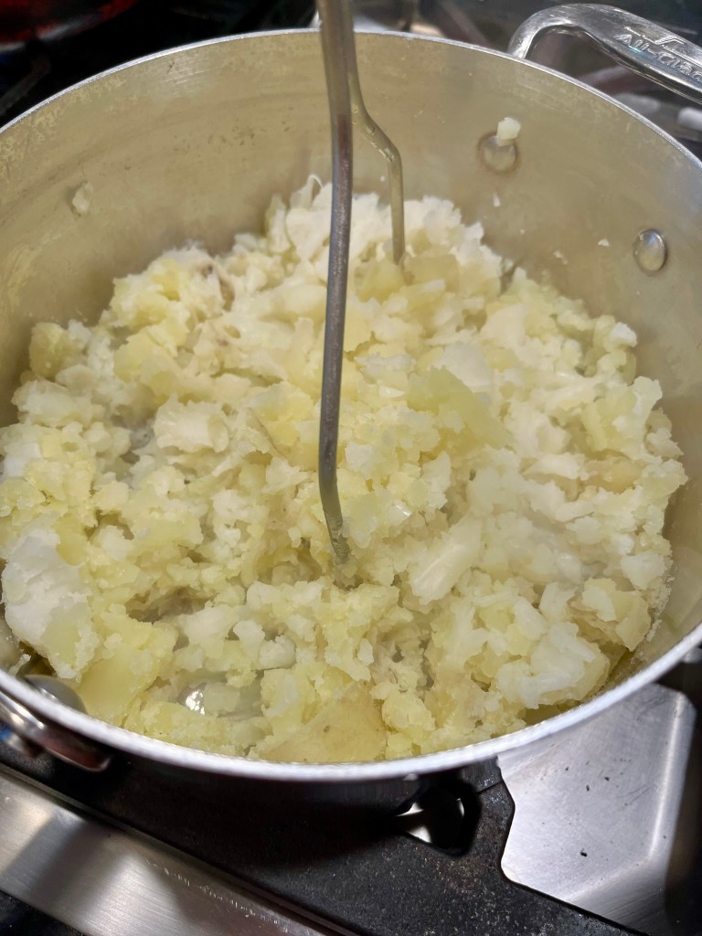 Pot of mashed potatoes being prepared with a mashing tool.
