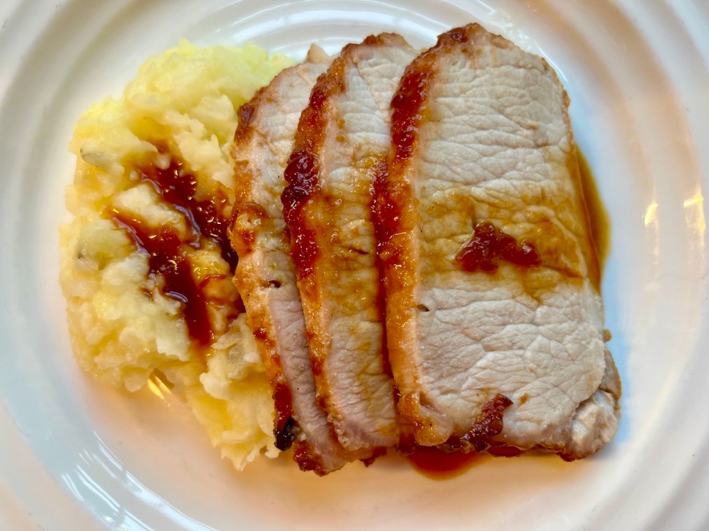 Sliced pork roast served with mashed potatoes and a drizzle of cherry sauce on a white plate.