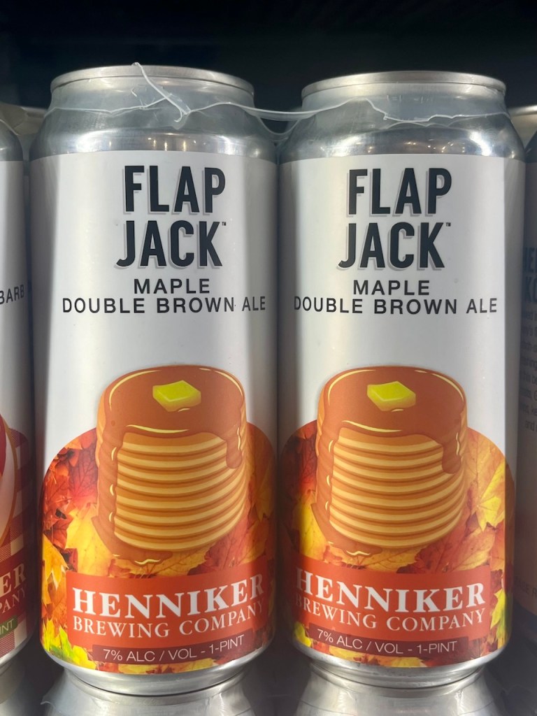 Cans of Flap Jack Maple Double Brown Ale from Henniker Brewing Company, featuring a design with pancakes and autumn leaves.