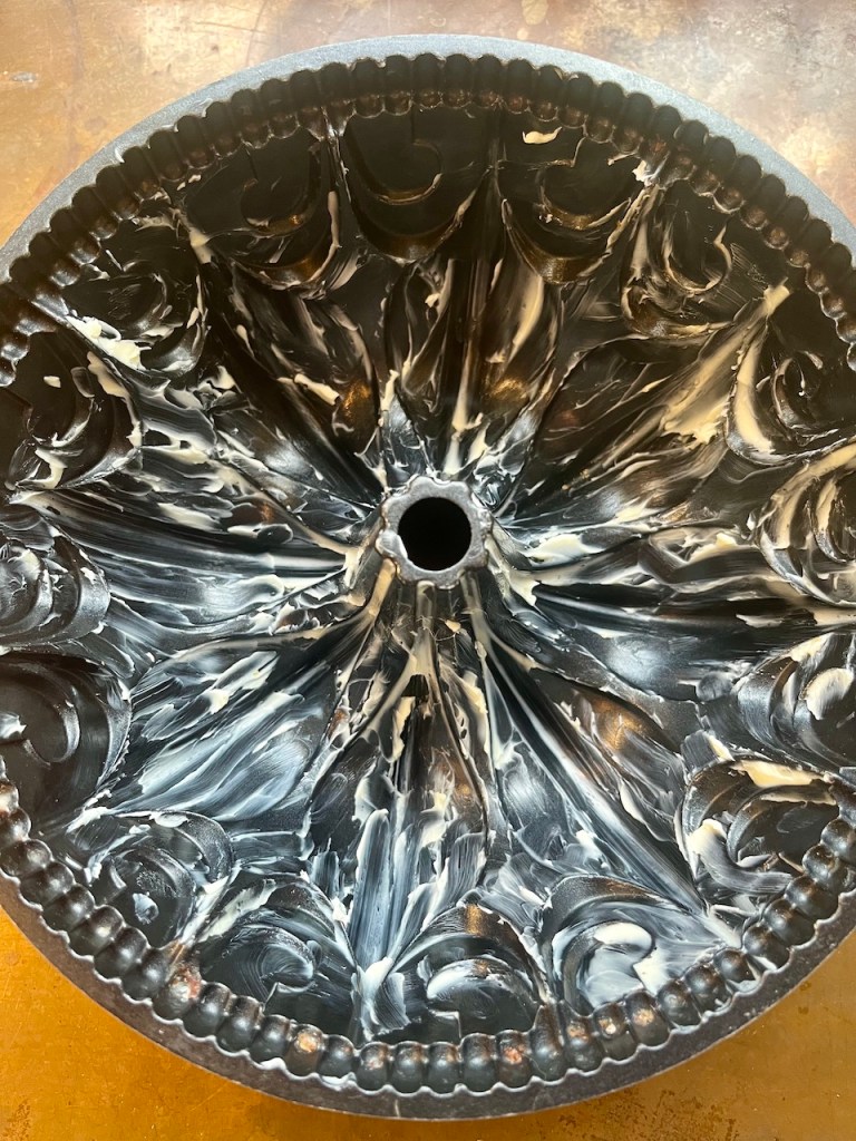A heavily greased bundt pan with a intricate design, prepared for baking.