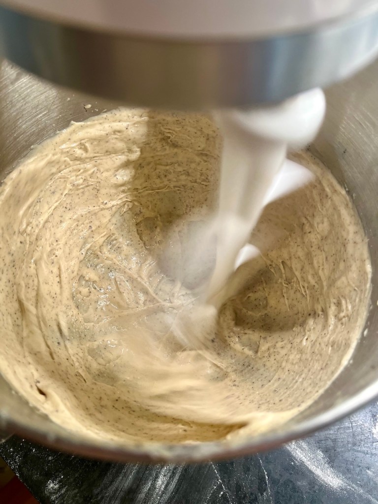 Close-up view of a mixing bowl containing a creamy batter, being stirred by a stand mixer.