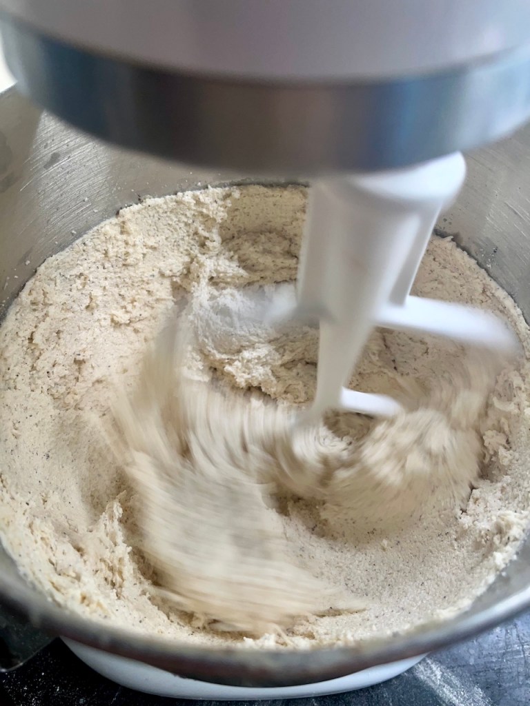 Close-up of a mixing bowl with flour and other ingredients being mixed by a stand mixer.