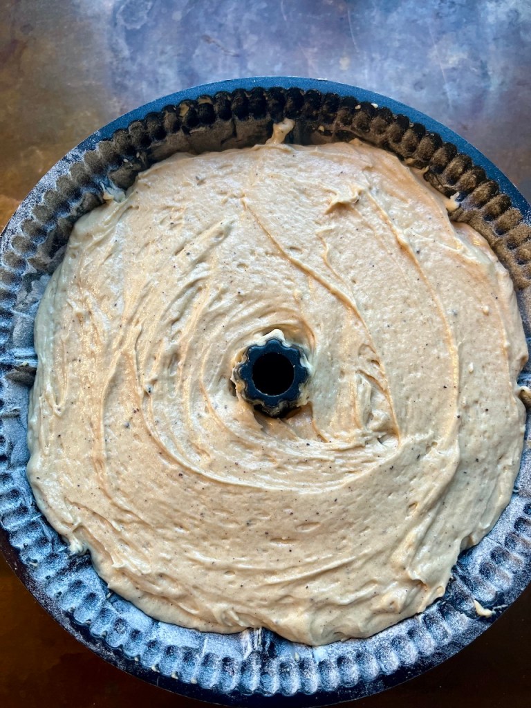 A bundt pan filled with uncooked burnt butter cider cake batter, ready for baking.
