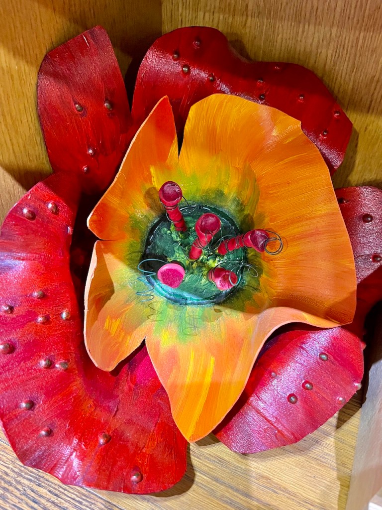 Artistic wooden flower sculpture with vibrant orange petals and red accents, featuring green details in the center.