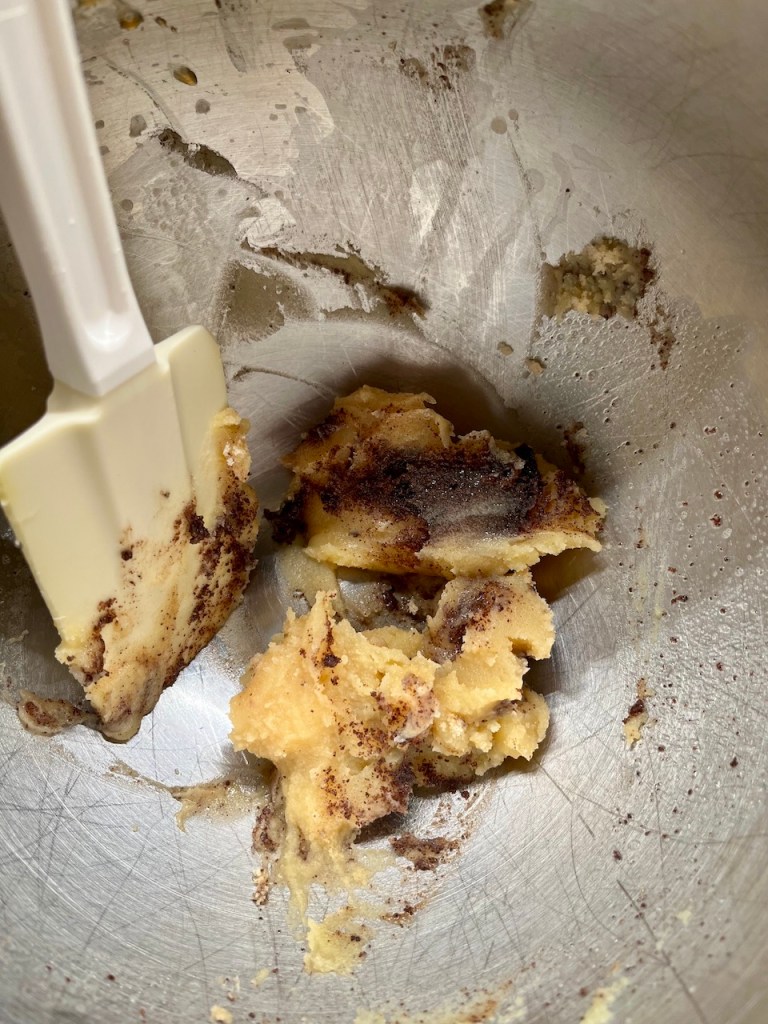 Mixing bowl with a mixture of cookie dough, showing chunks of burnt butter and sweetened batter.