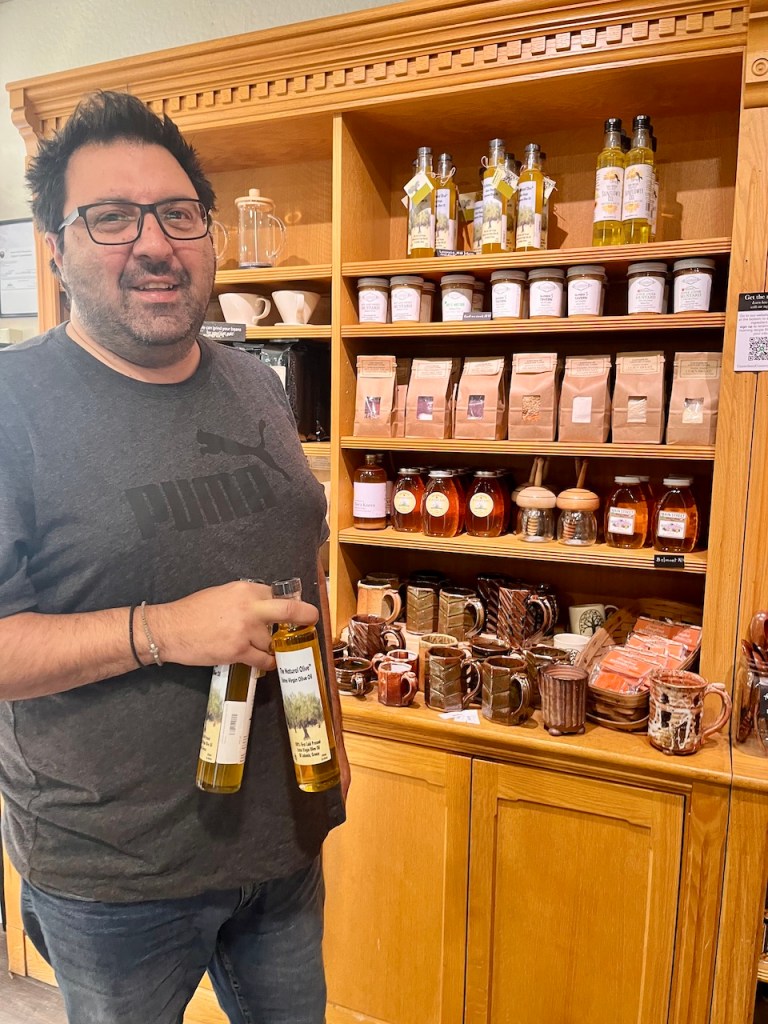 Man holding bottles of olive oil in a store, with shelves displaying various products in the background.