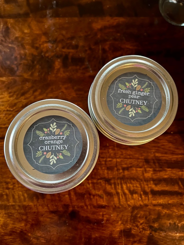 Two jars of chutney labeled 'fresh ginger pear chutney' and 'cranberry orange chutney' on a wooden surface.
