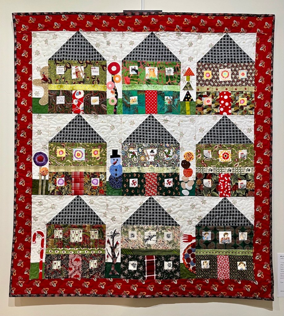 Colorful quilt featuring a pattern of houses with various designs, including snowmen and candy canes, bordered in red.