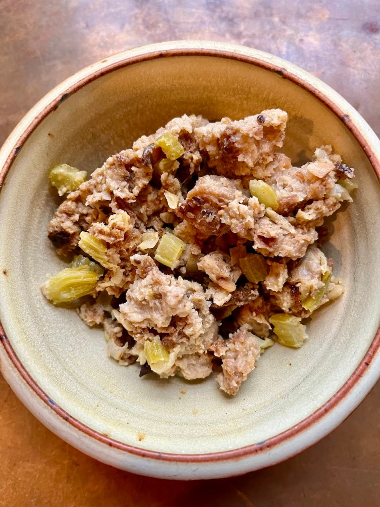 A bowl containing a serving of savory stuffing made with bread, celery, and seasonings.