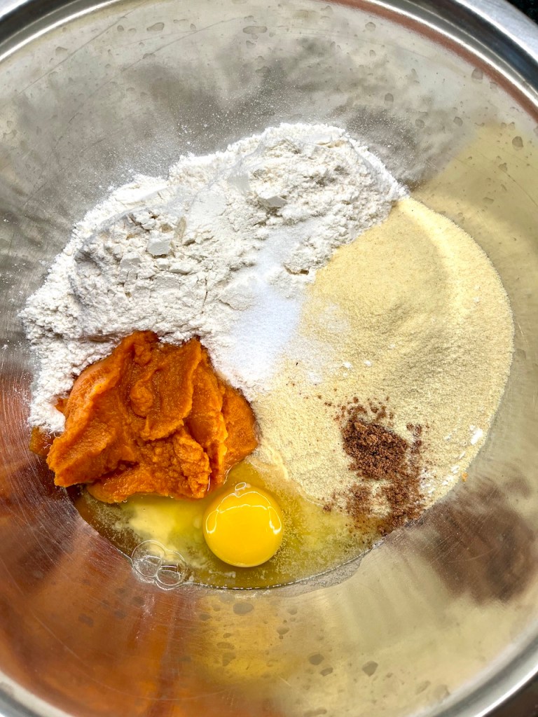 Ingredients for pumpkin gnocchi including flour, semolina, canned pumpkin, egg, salt, and nutmeg in a mixing bowl.