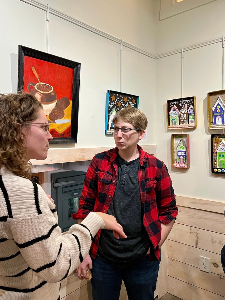 Two people engaged in conversation in an art gallery, with various artworks displayed on the walls.