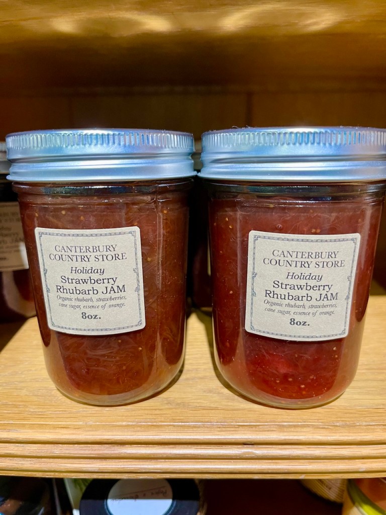 Two jars of Holiday Strawberry Rhubarb Jam on a wooden shelf, labeled with 'Canterbury Country Store' and details about the ingredients.