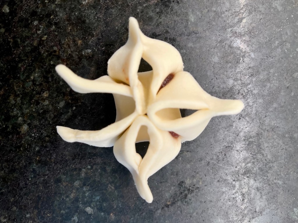 Top view of a decorative pastry shaped like an octopus or flower, with curled ends and a smooth surface, resting on a dark countertop.