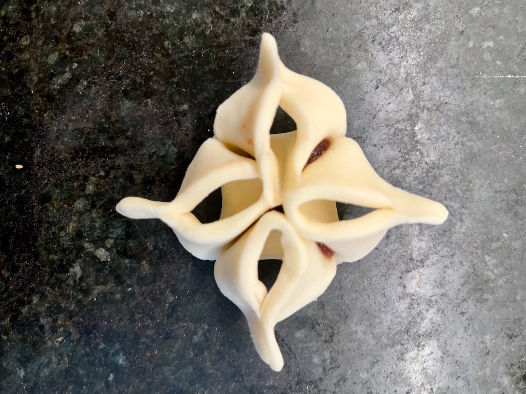An artistic pastry shape resembling a flower or star, with a light-colored, dough-like texture, placed on a dark granite surface.