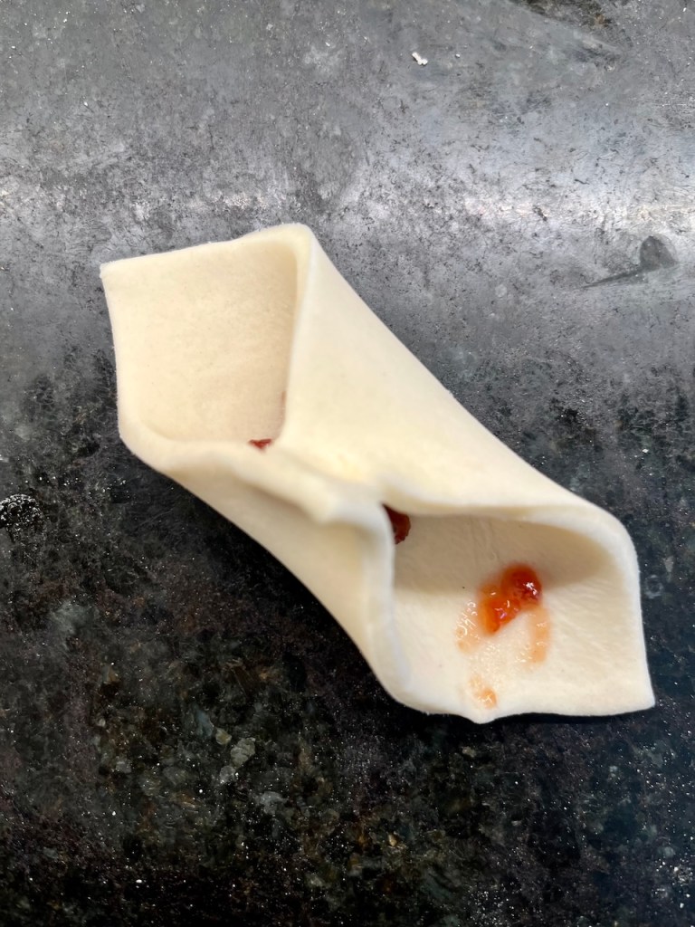 A folded piece of dough with a small amount of red sauce inside, resting on a dark countertop.