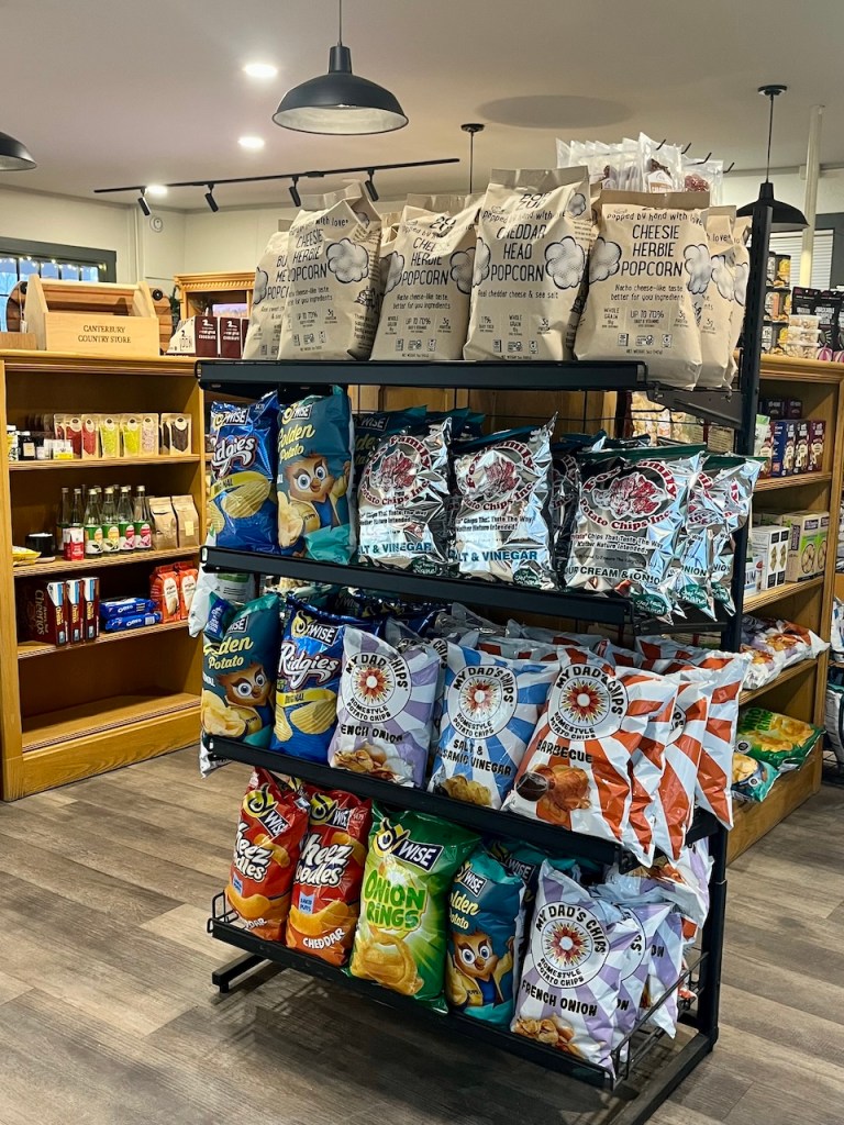 A display shelf in a store featuring various bags of snacks, including popcorn and potato chips, arranged neatly with some pantry items visible in the background.