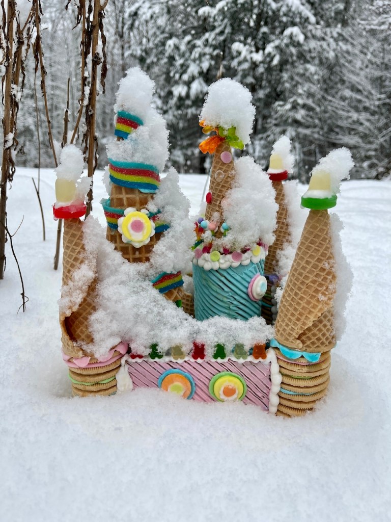 A whimsical ice cream cone castle adorned with colorful candy decorations, partially covered in snow, surrounded by a winter landscape.