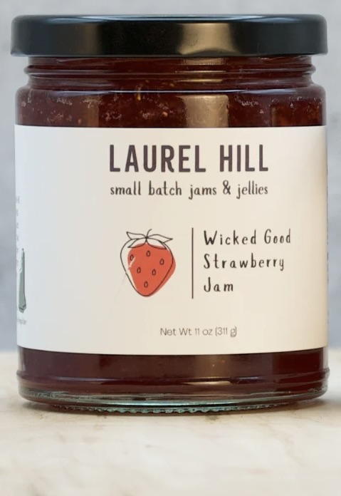 A jar of Laurel Hill Wicked Good Strawberry Jam, showcasing a label with a strawberry illustration and the text 'small batch jams & jellies'.